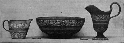 A cream jug, basin, and milk jug in jasper ware. The ground of these beautiful specimens is lilac, with Roman scroll ornament in white, and wreath of olive leaves From the South Kensington Museum